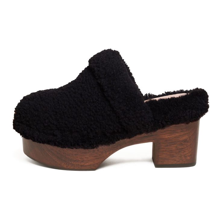 Side view of black shearling clog with sculpted wooden heel by Marie Laffont. 